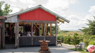 The outside of The Keep at Woodcock Smokery, a large wooden hut surrounded by fields and flowers
